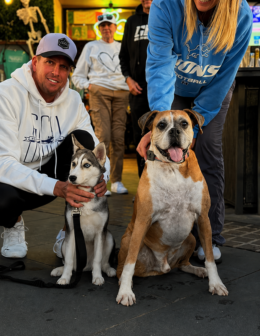 Two guests kneeling on the patio with their husky puppy and boxer mix at golden hour