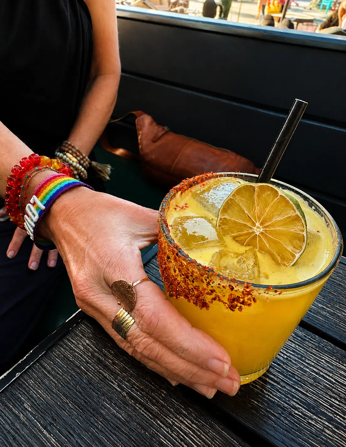 A hand holding a chili-salt-rimmed amber cocktail garnished with a dehydrated lime wheel.